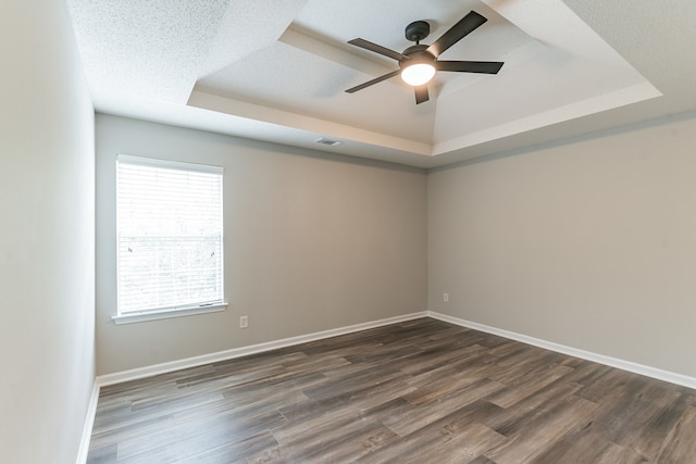 empty room featuring a tray ceiling, ceiling fan, dark hardwood / wood-style flooring, and a textured ceiling