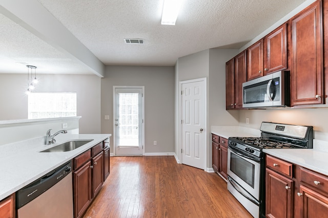 kitchen featuring pendant lighting, sink, light wood-type flooring, a textured ceiling, and appliances with stainless steel finishes