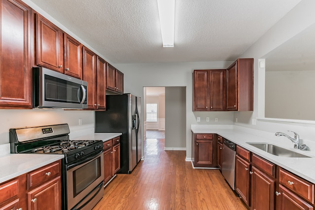 kitchen with a textured ceiling, sink, appliances with stainless steel finishes, and light hardwood / wood-style flooring