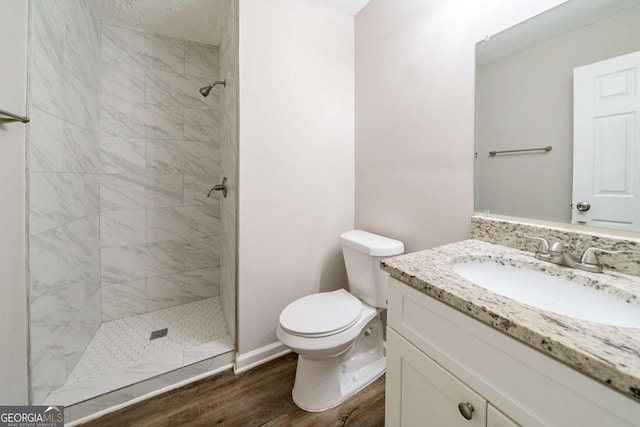 bathroom featuring hardwood / wood-style floors, a textured ceiling, tiled shower, toilet, and vanity