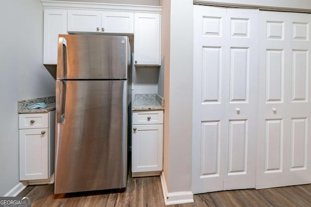 kitchen with white cabinets, stainless steel refrigerator, dark wood-type flooring, and light stone counters