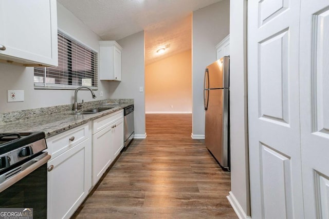 kitchen with light stone countertops, appliances with stainless steel finishes, sink, hardwood / wood-style floors, and white cabinetry