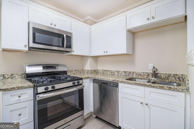 kitchen with sink, light stone countertops, ornamental molding, appliances with stainless steel finishes, and white cabinetry