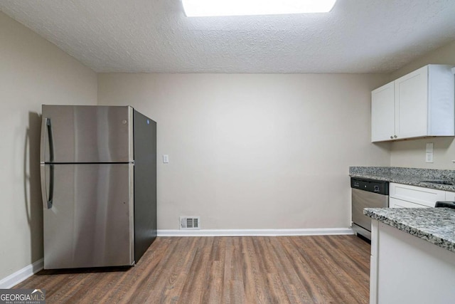 kitchen with light stone counters, a textured ceiling, stainless steel appliances, dark wood-type flooring, and white cabinets