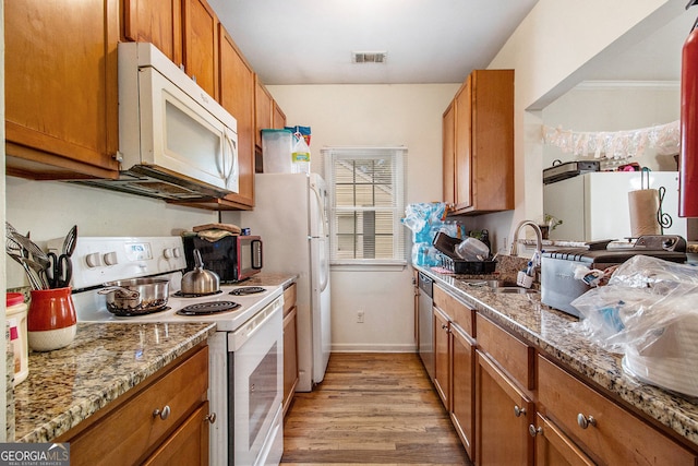 kitchen with light stone counters, white appliances, sink, and light hardwood / wood-style flooring