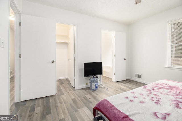 bedroom with ceiling fan, light hardwood / wood-style floors, a textured ceiling, a walk in closet, and a closet