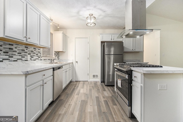 kitchen with island exhaust hood, tasteful backsplash, a textured ceiling, stainless steel appliances, and white cabinetry