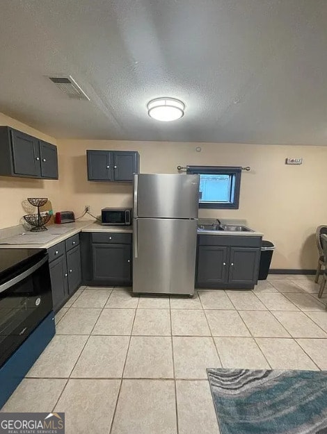 kitchen with appliances with stainless steel finishes, a textured ceiling, light tile patterned floors, and sink