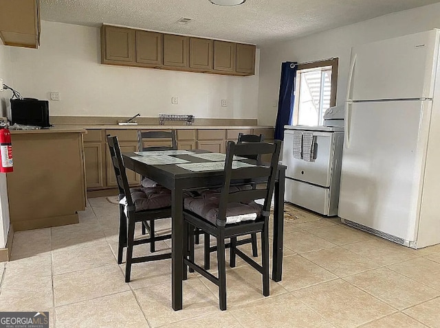 kitchen featuring stove, light tile patterned floors, a textured ceiling, and white refrigerator