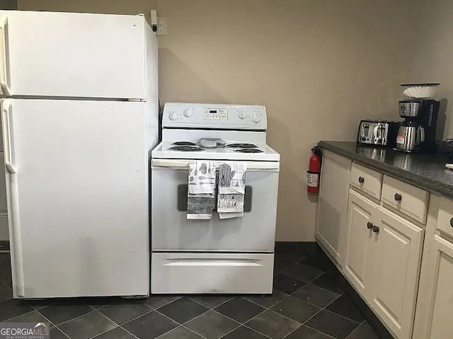 kitchen featuring cream cabinets, dark tile patterned flooring, and white appliances