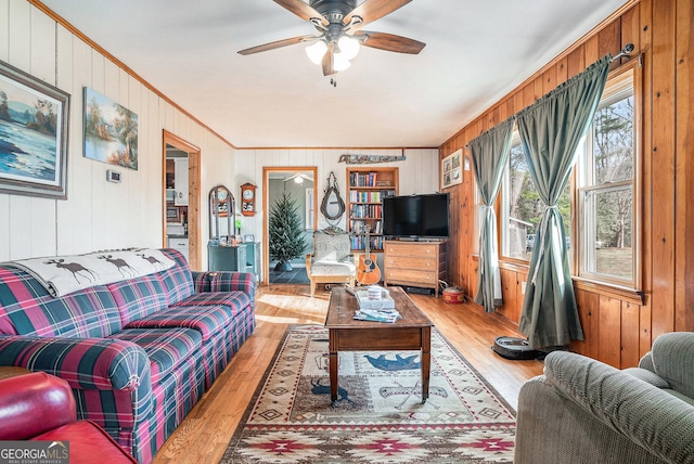 living room with wooden walls, ceiling fan, ornamental molding, and light wood-type flooring