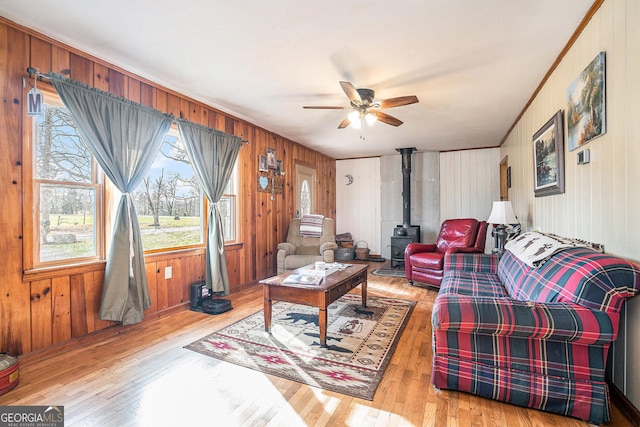 living room featuring wood walls, a wood stove, crown molding, ceiling fan, and light wood-type flooring