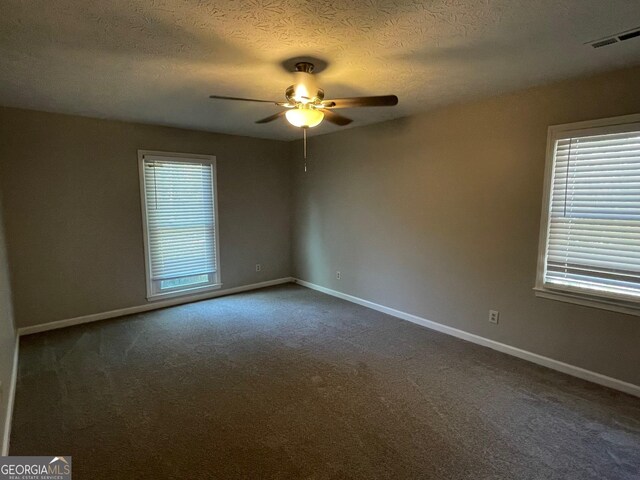 empty room with ceiling fan, dark carpet, and a textured ceiling