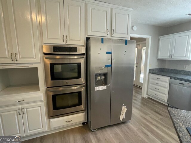 kitchen with white cabinets, stainless steel appliances, a textured ceiling, and light wood-type flooring