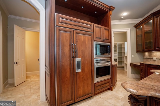 kitchen featuring light stone countertops, appliances with stainless steel finishes, backsplash, and ornamental molding