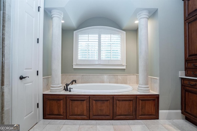 bathroom with a washtub, tile patterned floors, vaulted ceiling, and ornate columns