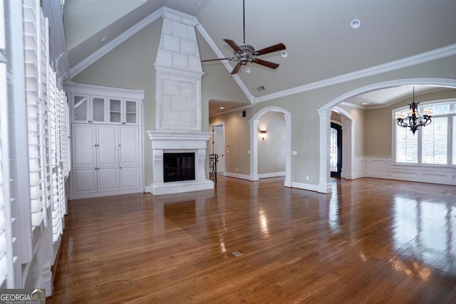 unfurnished living room with ornamental molding, ceiling fan with notable chandelier, dark wood-type flooring, high vaulted ceiling, and a fireplace