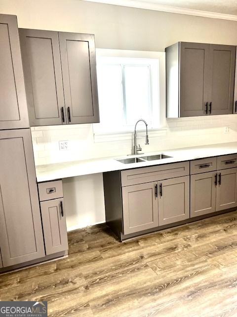 kitchen with sink, tasteful backsplash, light hardwood / wood-style flooring, gray cabinets, and ornamental molding