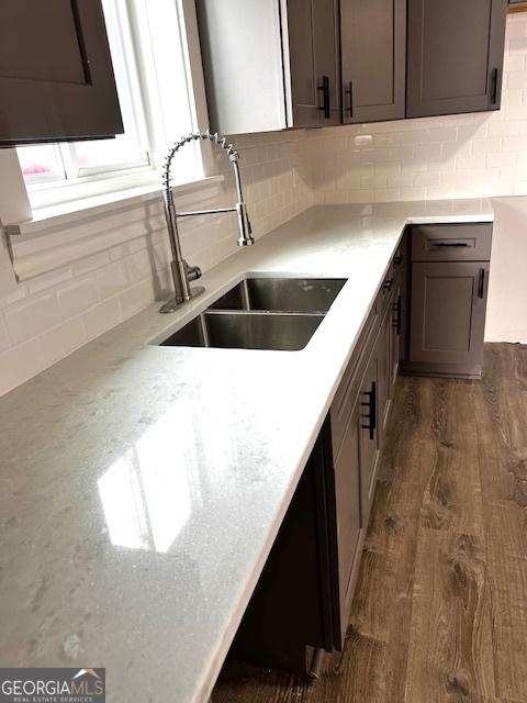 kitchen featuring light stone countertops, tasteful backsplash, dark brown cabinetry, dark wood-type flooring, and sink