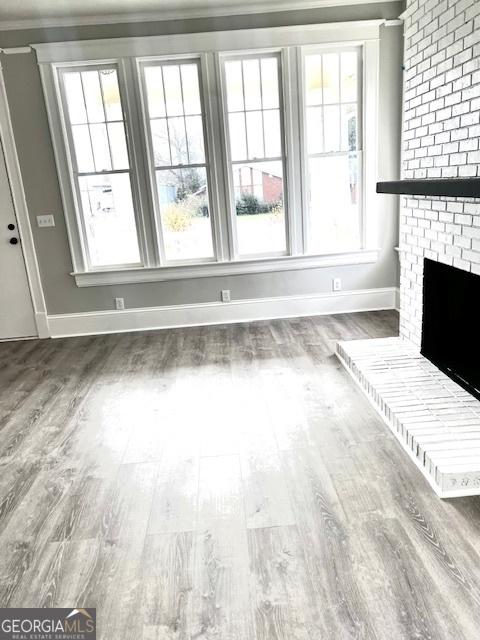 unfurnished living room featuring hardwood / wood-style floors, ornamental molding, and a brick fireplace