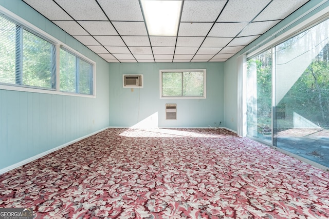 carpeted empty room with a drop ceiling and a wall unit AC