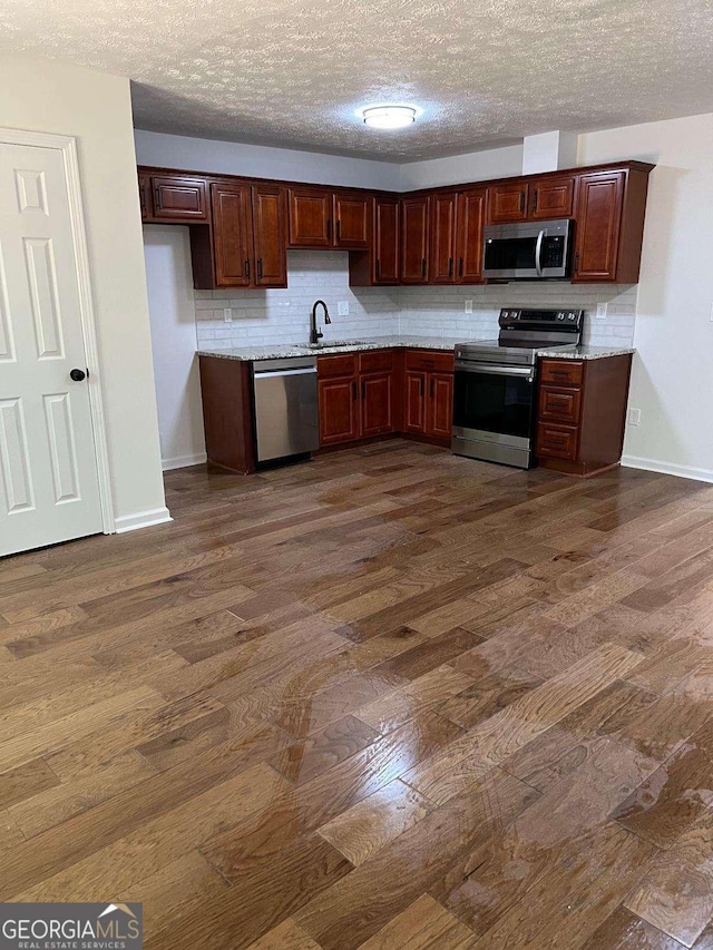 kitchen featuring sink, dark wood-type flooring, a textured ceiling, decorative backsplash, and appliances with stainless steel finishes