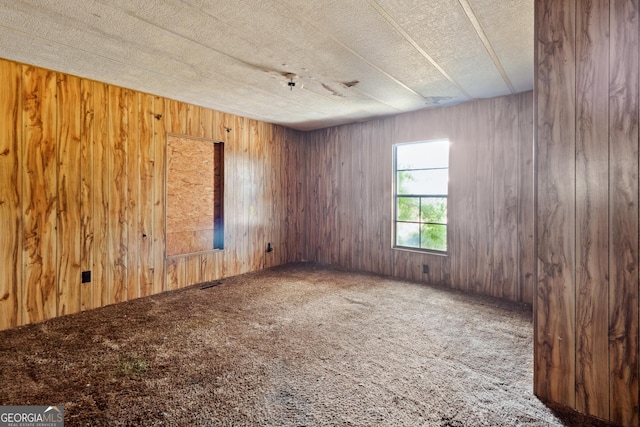 empty room with wood walls, carpet, and a textured ceiling