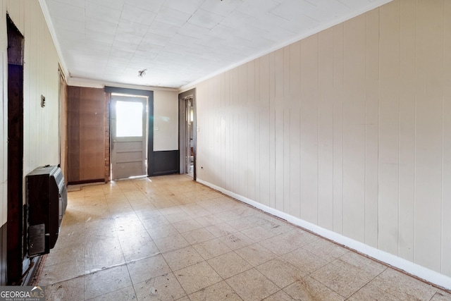 empty room featuring wood walls, crown molding, and heating unit