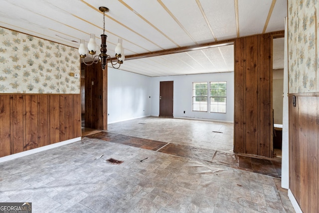 unfurnished room featuring wooden walls and a notable chandelier