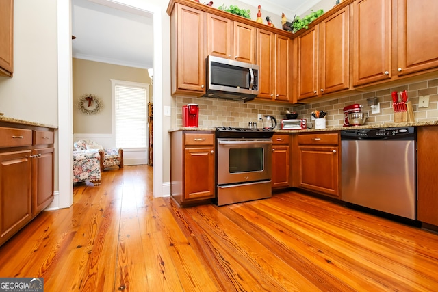 kitchen with brown cabinets, crown molding, stainless steel appliances, light wood-style floors, and light stone countertops