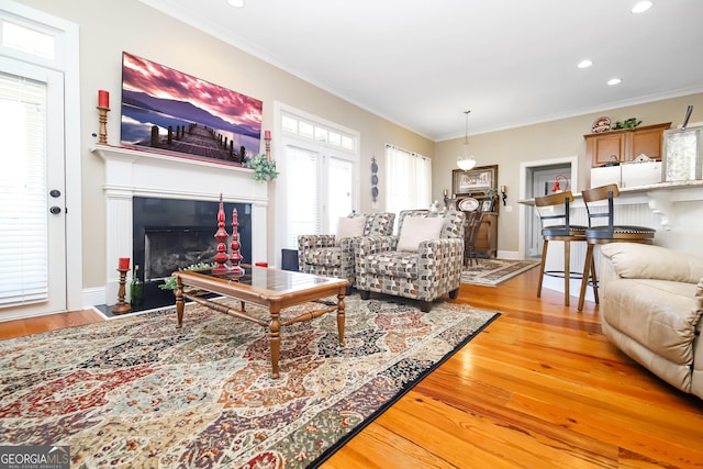 living room with a fireplace with flush hearth, light wood-type flooring, ornamental molding, and recessed lighting