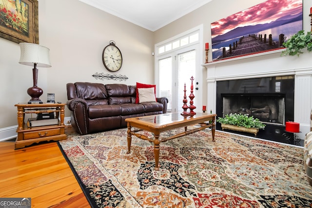 living room featuring a tile fireplace, crown molding, baseboards, and wood finished floors