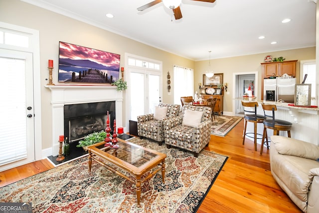 living area featuring light wood-type flooring, a fireplace with flush hearth, ornamental molding, and a wealth of natural light