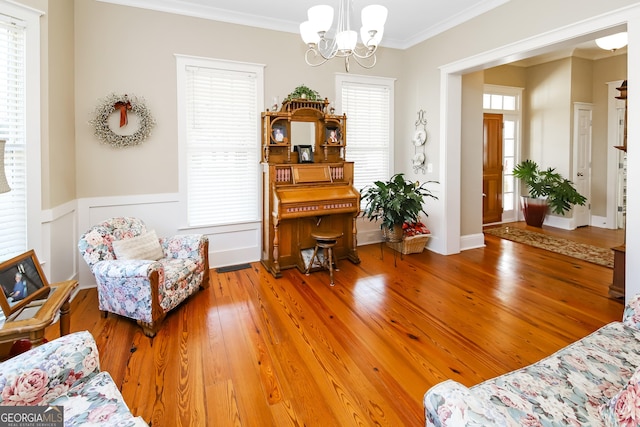 living area featuring ornamental molding, a chandelier, wainscoting, and wood finished floors