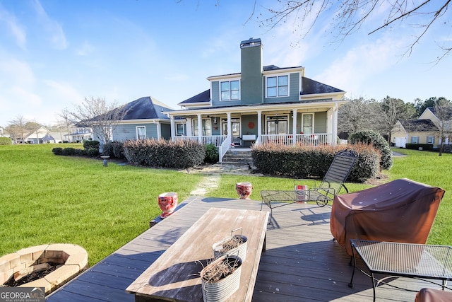 back of property featuring covered porch, an outdoor fire pit, a chimney, and a yard