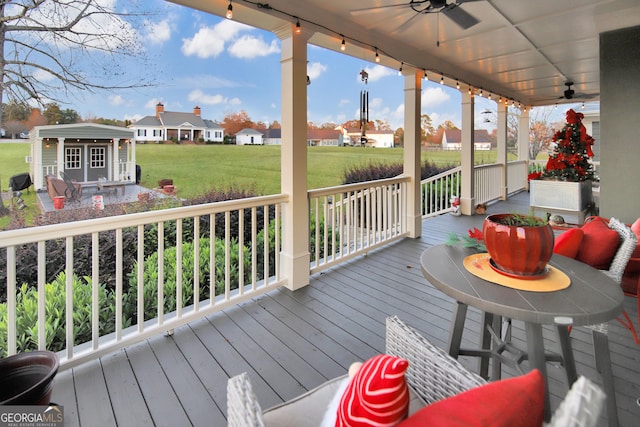 wooden deck featuring a lawn, ceiling fan, an outbuilding, and covered porch