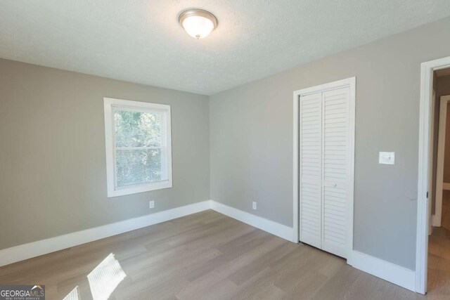 unfurnished bedroom with a textured ceiling, light hardwood / wood-style floors, and a closet