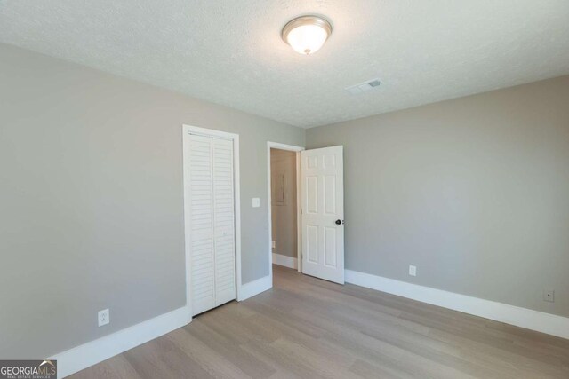 unfurnished bedroom with light wood-type flooring, a textured ceiling, and a closet