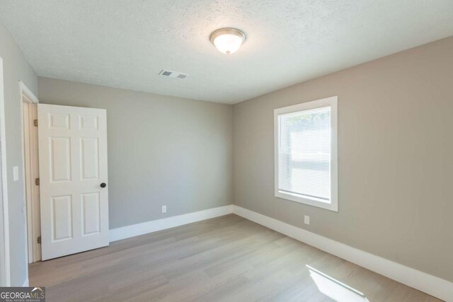 unfurnished room with a textured ceiling and light hardwood / wood-style floors