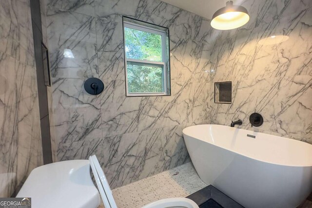 bathroom with a tub to relax in, toilet, and tile walls