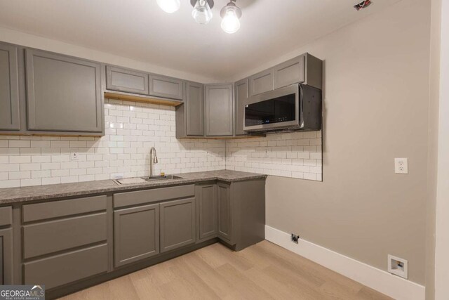 kitchen with gray cabinetry, sink, light hardwood / wood-style flooring, dark stone counters, and decorative backsplash