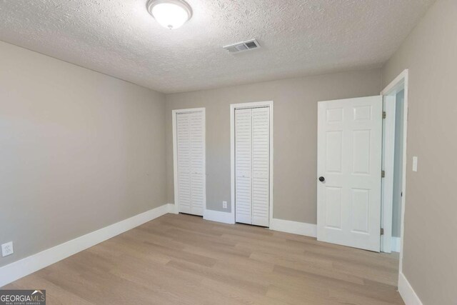 unfurnished bedroom featuring two closets, a textured ceiling, and light hardwood / wood-style flooring