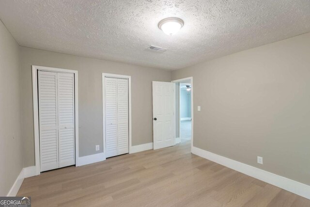 unfurnished bedroom featuring two closets, a textured ceiling, and light wood-type flooring