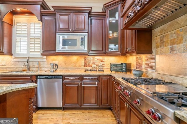 kitchen featuring light stone countertops, tasteful backsplash, light hardwood / wood-style floors, custom range hood, and appliances with stainless steel finishes