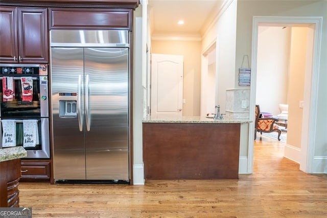 kitchen featuring double oven, built in refrigerator, light stone countertops, and light hardwood / wood-style floors