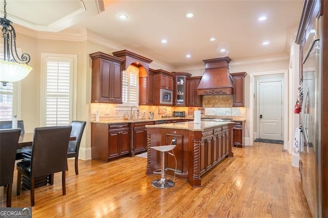 kitchen with backsplash, premium range hood, light hardwood / wood-style flooring, a center island, and stainless steel microwave