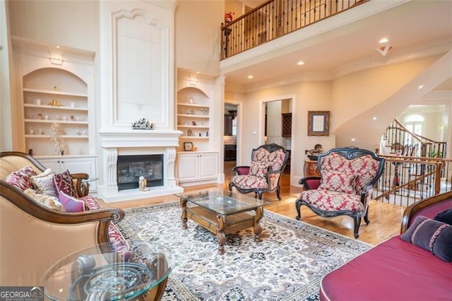 living room with a towering ceiling, a large fireplace, crown molding, built in features, and hardwood / wood-style floors