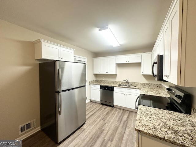 kitchen with sink, stainless steel appliances, light stone counters, light hardwood / wood-style floors, and white cabinets