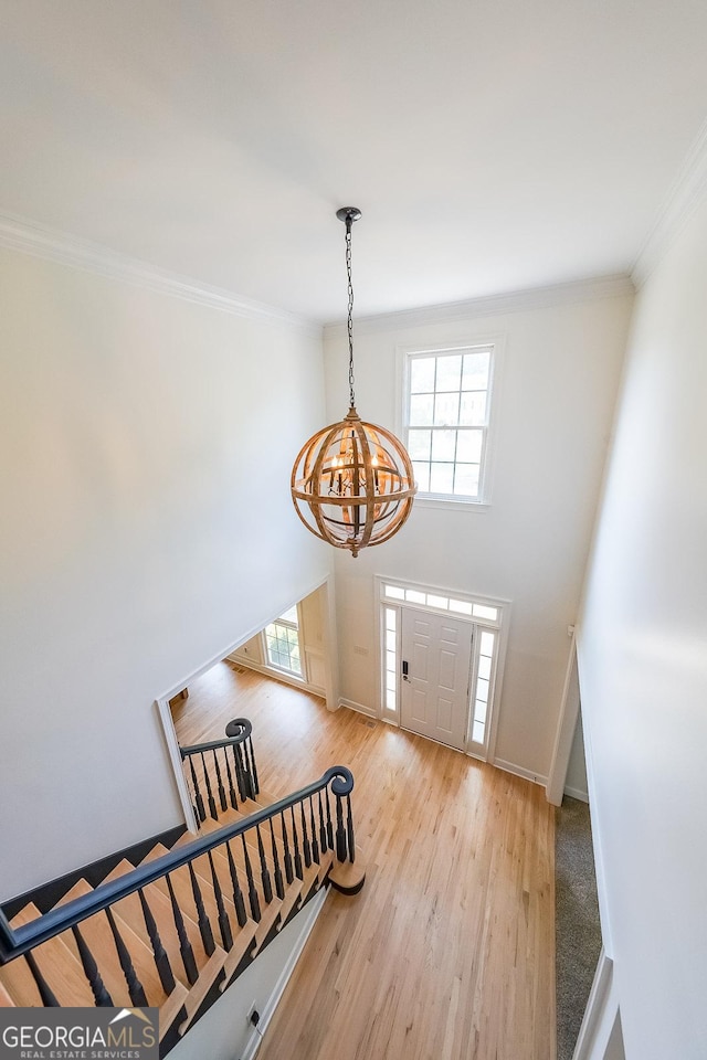 entryway with light wood-type flooring, crown molding, and an inviting chandelier