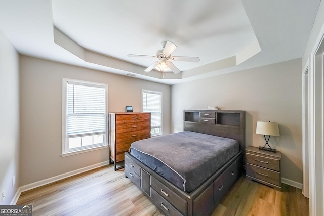 bedroom featuring light wood-type flooring, a tray ceiling, and ceiling fan